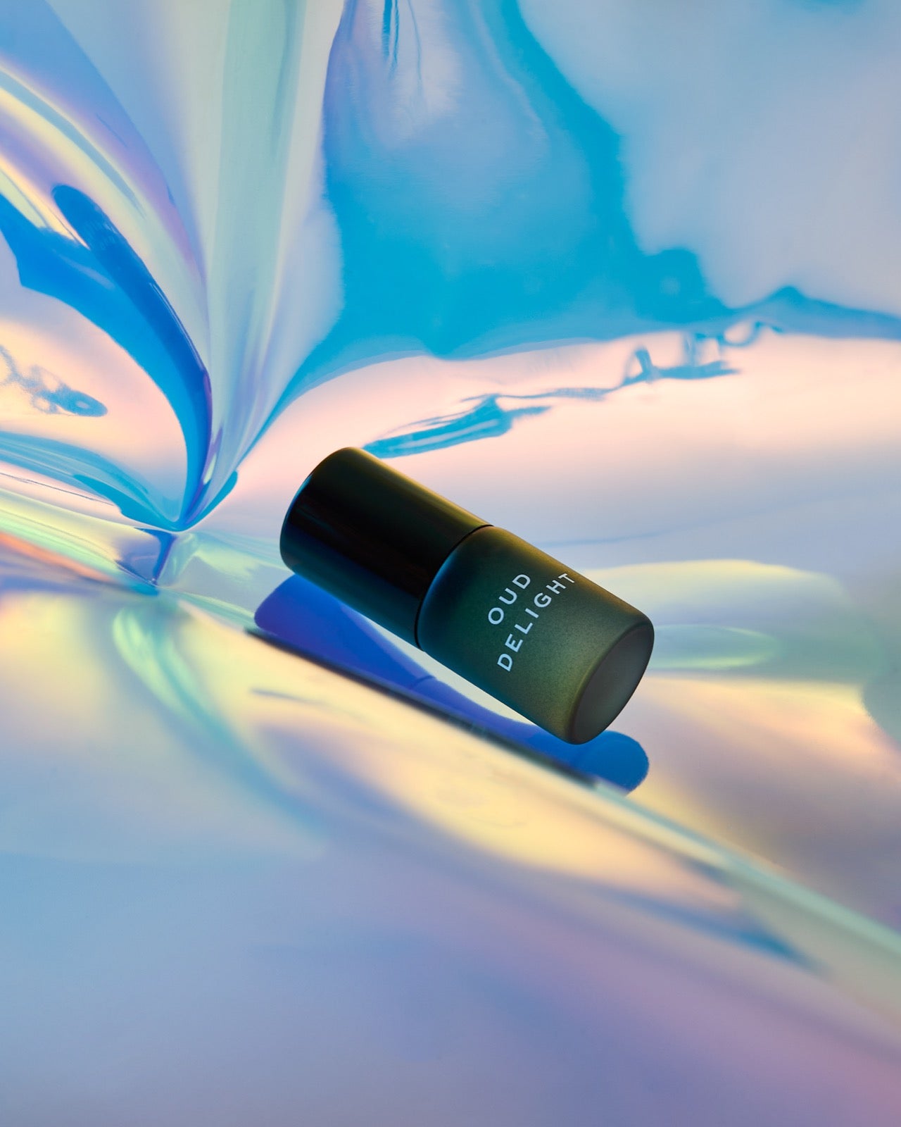 Dark Oud Delight mini bottle on an iridescent rain-blue backdrop