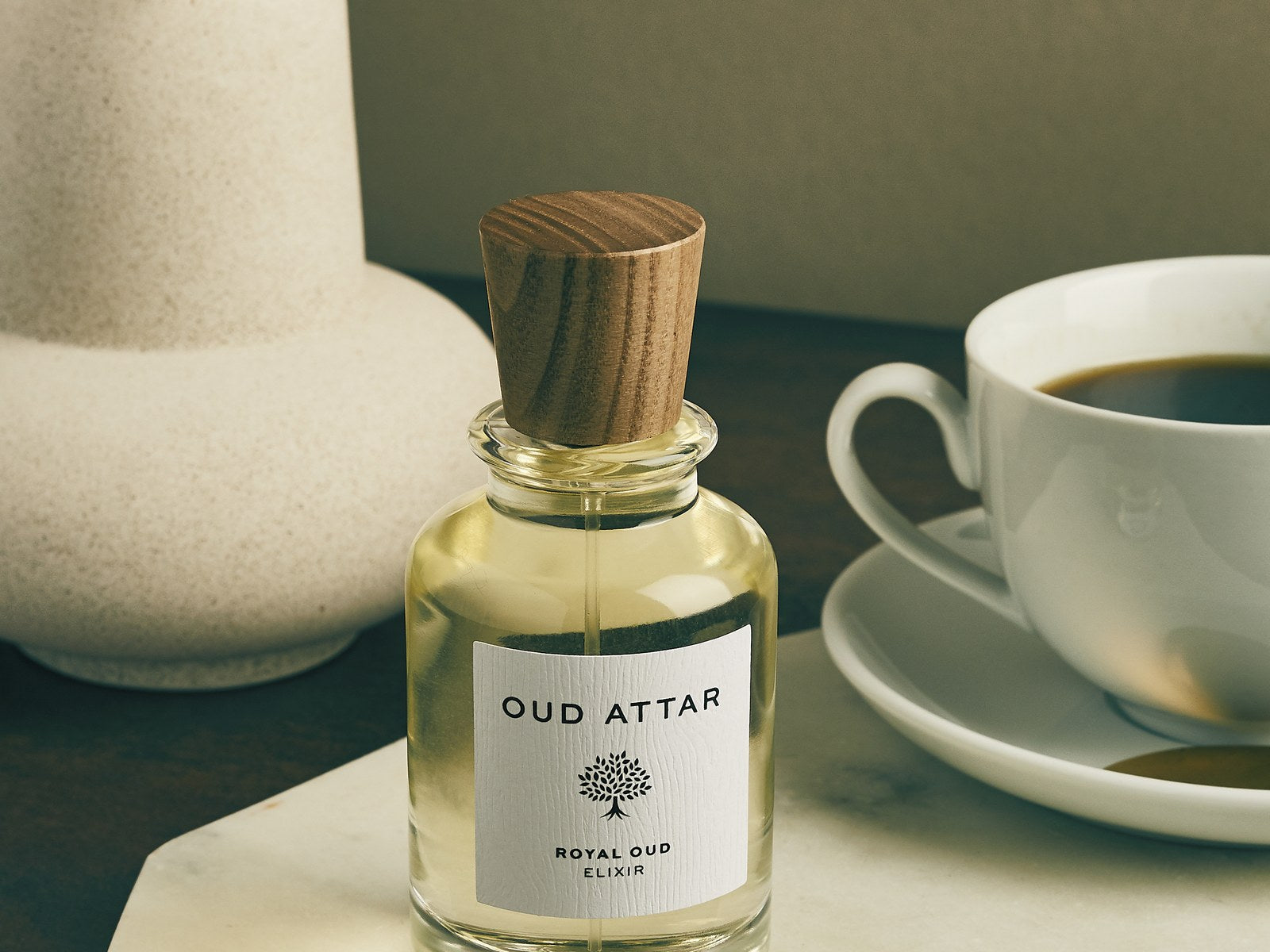 Royal Oud elixir beside a cup and saucer on marble