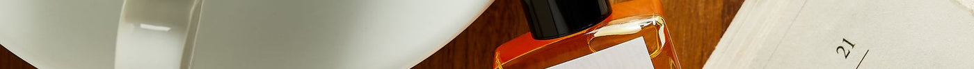 Spiced Oud perfume oil on an open book beside a cup of coffee and reading glasses