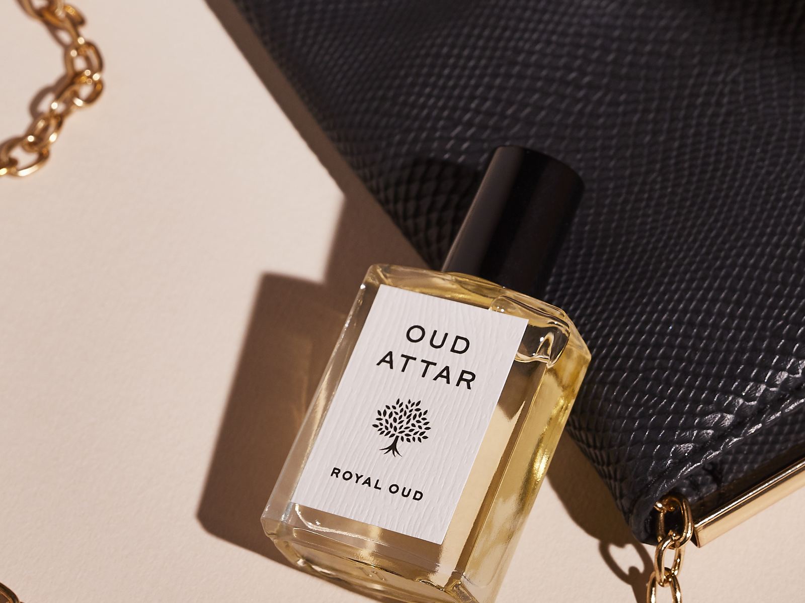 Royal Oud perfume oil resting on a black handbag with a gold chain