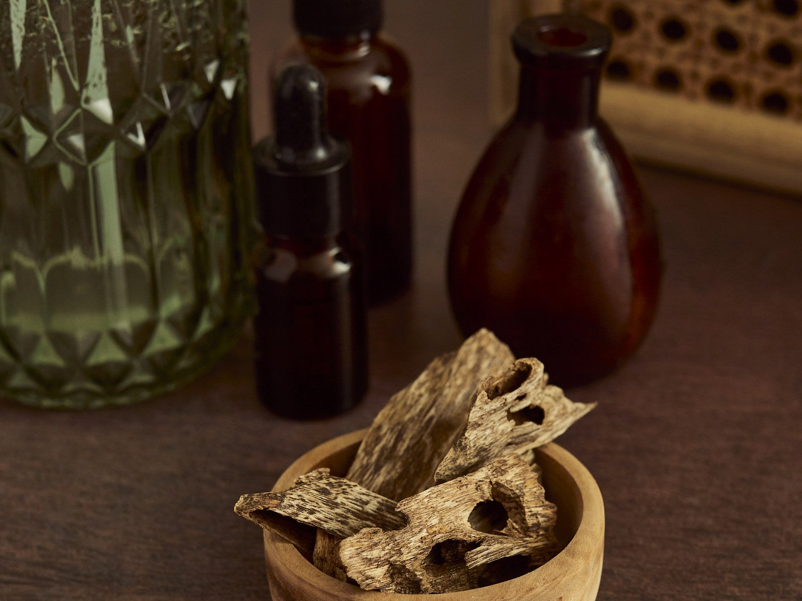 Agarwood chips in a wooden bowl with apothecary bottles